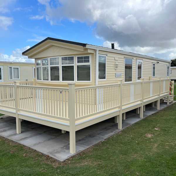 A fully constructed white and cream end patio deck with a walkway, steps and a gate, attached to a caravan