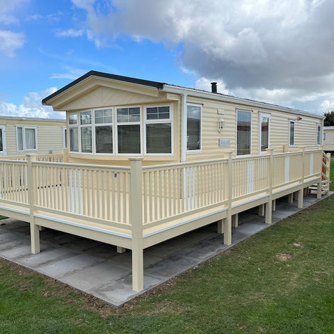 A fully constructed white and cream end patio deck with a walkway, steps and a gate, attached to a caravan