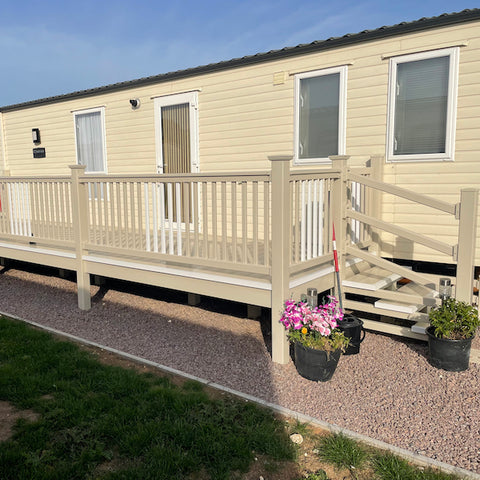 A fully constructed white and cream side patio deck with steps and a gate, attached to a residential mobile home.